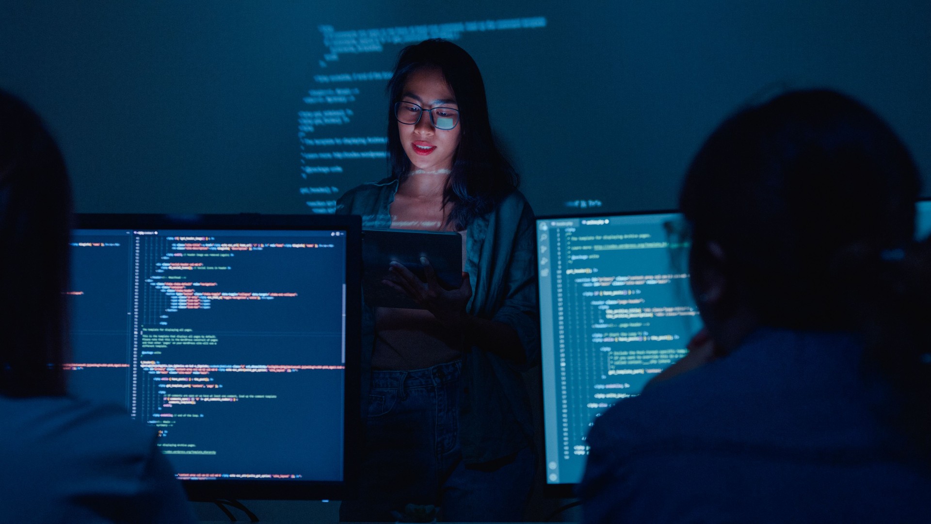 Young Asian woman software developers mentor leader manager talking to executive team analyzing source code in office at night.